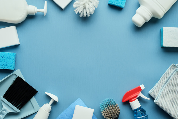 A round flatlay of white and blue pieces of toilet cleaning equipment and detergents on a blue surface