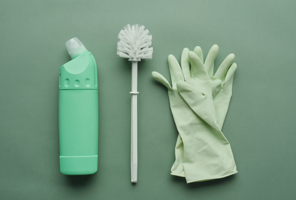 Green detergent bottle toilet brush and green rubber gloves on a green surface