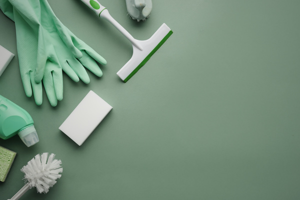Flatlay of green and white pieces of the cleaning set such as bottles with household chemicals window scraper and brushes