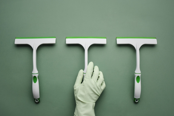 A green-and-white window brushes wiper lying in the middle of the same pieces is held by a hand in a green rubber glove