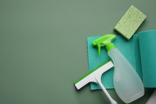 A window cleaning kit consisting of detergent in a sprayer viscose wipes in a sponge roll and window brushes wiper is laid out on a green surface