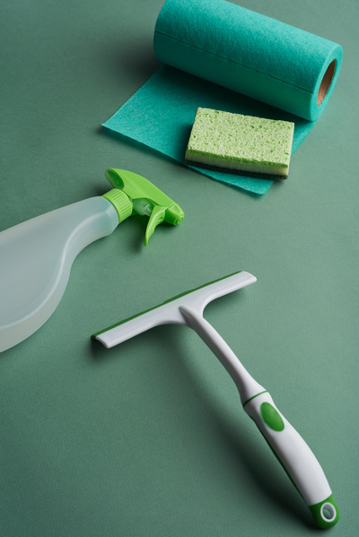 A window cleaning set consisting of detergent in a spray sponge viscose napkins in a roll and window brushes water is scattered on a green surface