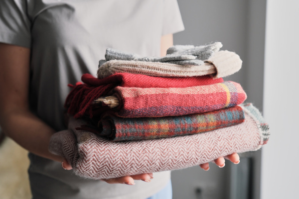 Neatly folded knitted warm clothes are held by a woman in a light T-shirt with two hands