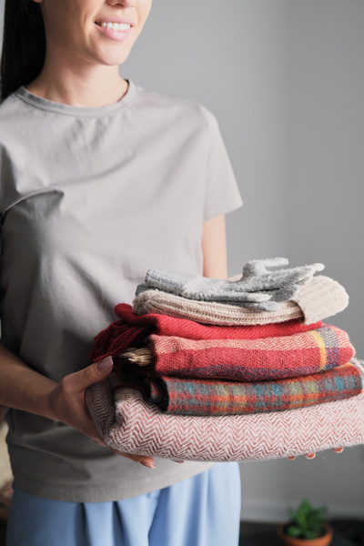A neatly folded stack of warm clothes in the hands of a smiling woman in a light T-shirt