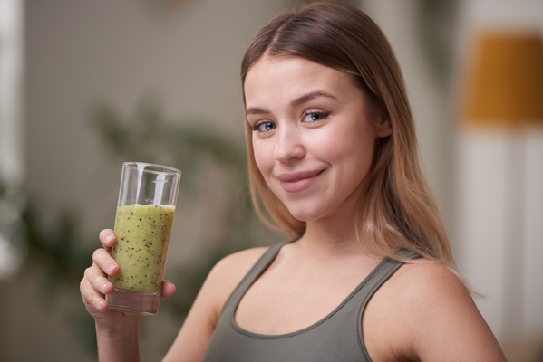 Athletic woman with dyed hair wearing a sports top smiling holding a green smoothie