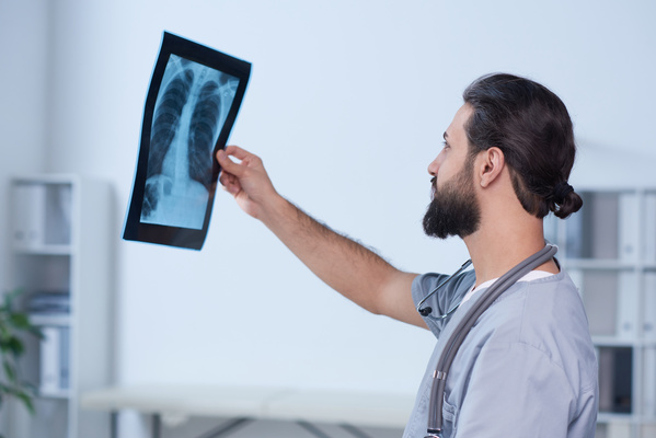 A male doctor in uniform examines the results of an X-ray of the patient thoracic region
