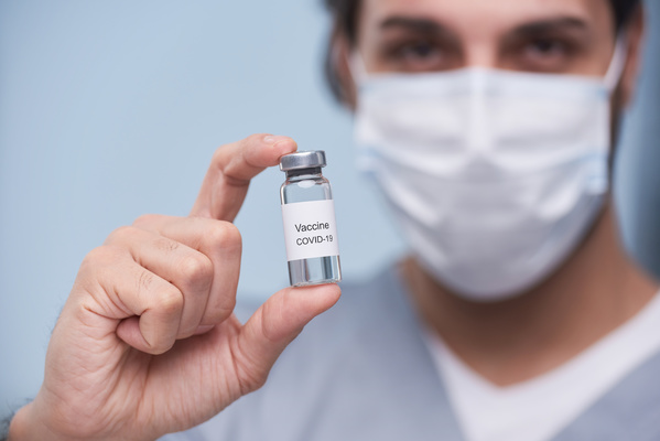 A small injection bottle with a medicine is in the hand of a doctor in medical mask