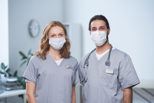 Two doctors in medical masks and gray uniforms with badges standing next to each other