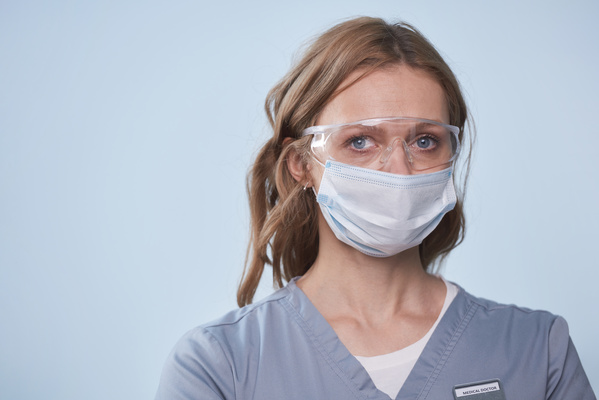 A female doctor dressed in a uniform with a medical mask and protective glasses on her face