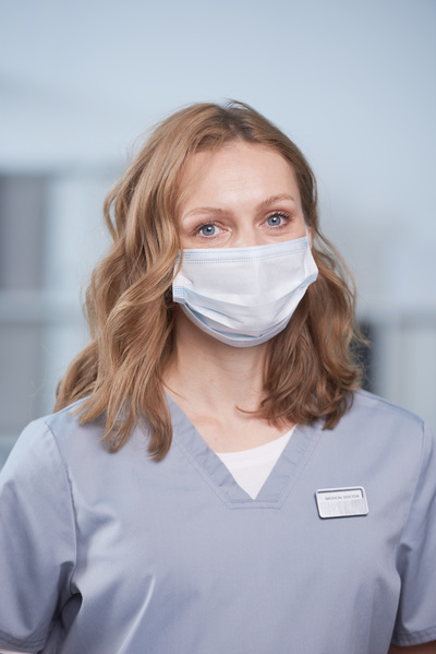 Portrait of a female medic with brown curly hair and a medical mask on her face dressed in a gray uniform in the office