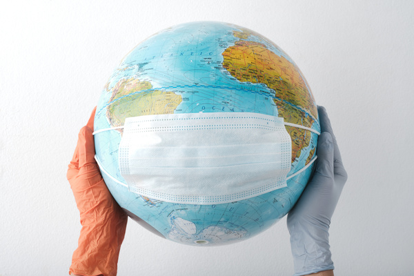 Globe with a mask on it is in the hands of orange and blue rubber gloves