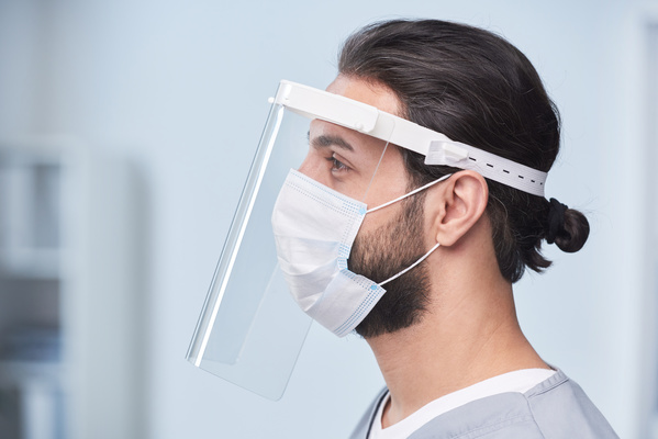 Profile of a male doctor wearing uniform and a plastic screen and a medical mask