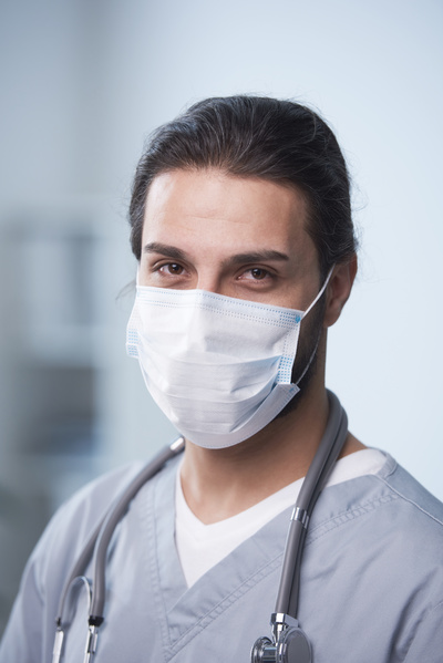 A male physician with brown eyes wearing a disposable medical mask with a stethoscope around his neck