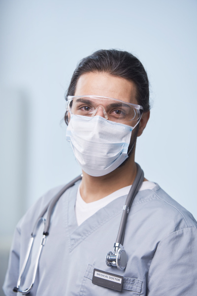 Portrait of a male doctor with brown eyes and with medical protection on his face in the form of a disposable mask and protective glasses