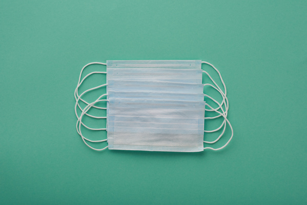 Unused disposable medical masks are laid out on a turquoise surface