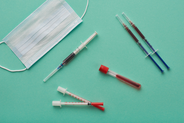 A medical set for blood collection comprising syringes test tubes and a disposable mask lying on a turquoise background
