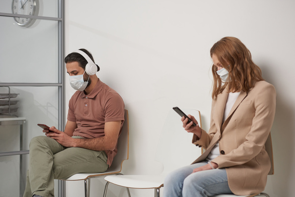 Patients with headphones and phones in their hands waiting for a appointment with a doctor in the corridor
