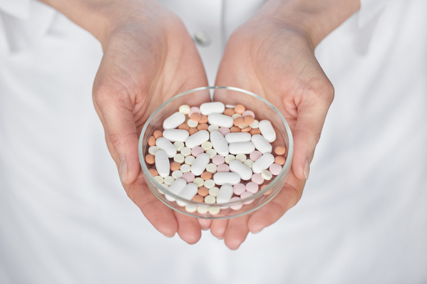 A glass round petri dish with pills of different shapes and colors is held by a doctor