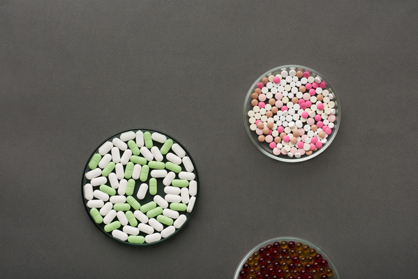 Round glass petri dish with round pills of different colors on a pink surface