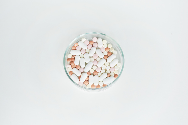 Round transparent petri dish with pills of different colors and shapes on a white surface