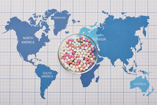 Round transparent petri dish full of pills of different colors on the world map
