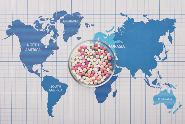 Round transparent petri dish with medicine of different colors on the world map