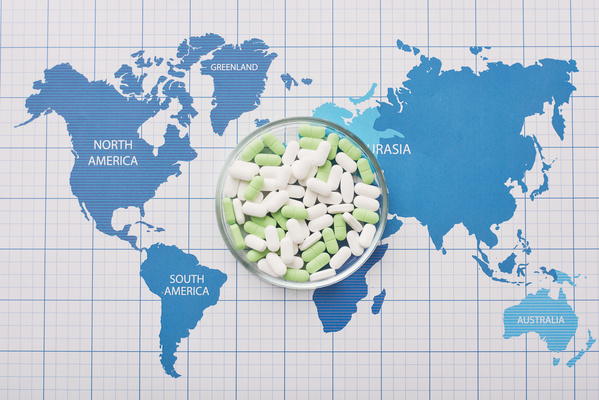 Round transparent petri dish with oval pills of green and white colors on the world map