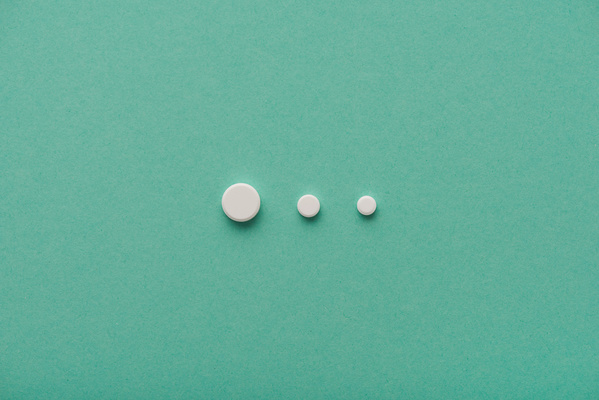 Three white round pills are arranged in decreasing order of size on a turquoise surface