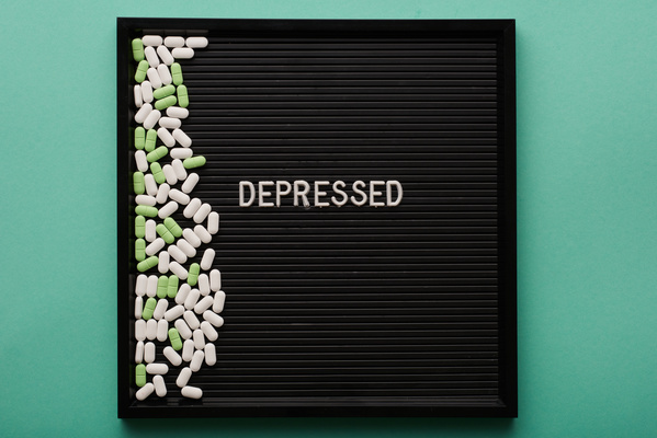 A black ribbed tray with white and green oval pills scattered on the left side and with a white lettering depressed is on the turquoise surface