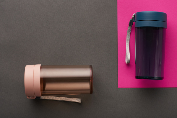 Plastic sports water bottles in black and pink colors lie on surfaces of contrasting shades