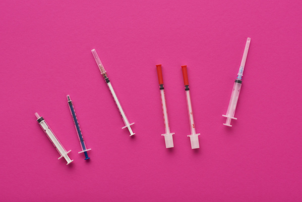 Empty syringes of different sizes are scattered on the surface of a bright pink color