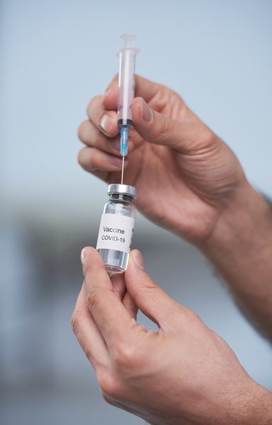 A close-up of a vaccine from an vial that is injected into a small volume hypodermic with hands