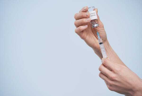 An inverted ampoule with a vaccine pierced with a small syringe to inject the medicine into it is held in the hands