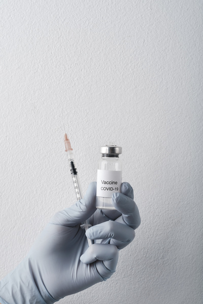 The vaccine in an ampoule and a syringe are held with a hand in a rubber medical glove on a white background