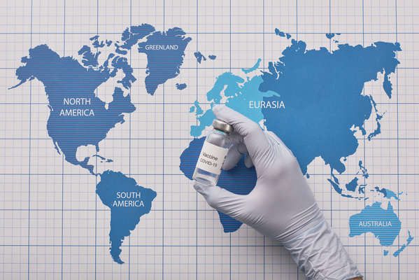 Vaccine in an ampoule in the hand in a rubber medical glove on the background of the world map