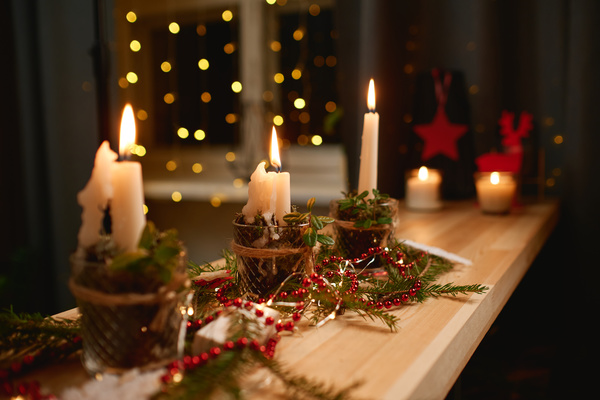 A Christmas composition of burning candles in candlesticks beads and twigs of spruce stands on the table in cozy lighting