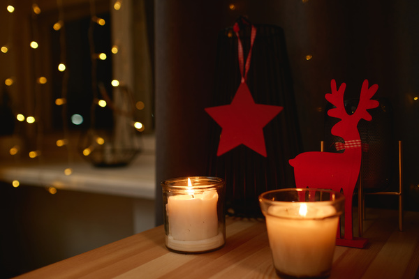 Candles in glass candlesticks stand on a table with a red deer figurine and a star hanging on a vase creating a Christmas atmosphere