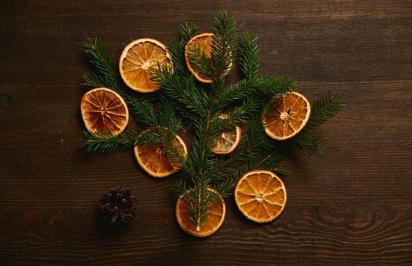 Christmas composition of a fir branch and orange slices on a dark wood table next to a fir cone