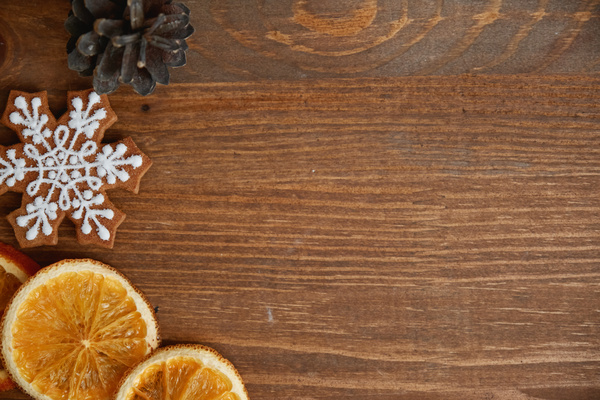 Dried slices of orange gingerbread with icing in the shape of a snowflake and a fir cone are laid out on a wooden table