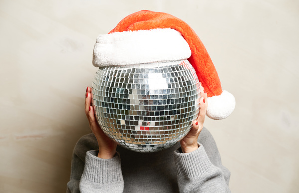 A woman in a light gray sweater hid her head behind a large disco ball with a red Santa hat