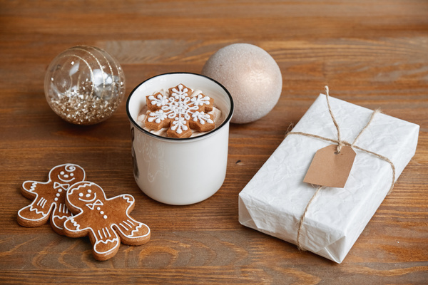 Cocoa with a gingerbread snowflake on top in a white mug on a wooden table with gingerbread men a Christmas gift in a white wrapper and Christmas baubles with sequins