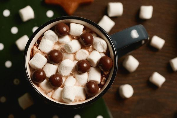 Cocoa with marshmallows and chocolate balls in a dark-colored mug on a background of marshmallows scattered on wrapping paper