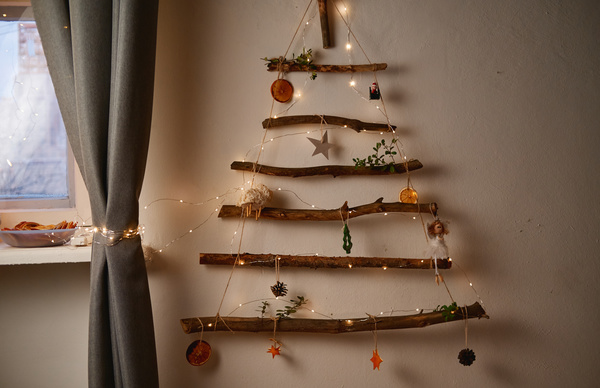Christmas decoration on the wall in the form of a Christmas tree made of small logs decorated with a garland Christmas toys and dried fruits