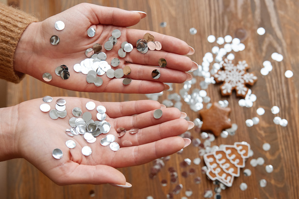Silver confetti scattered on female hands and over a wooden table with Christmas gingerbread