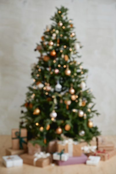 A blurry photo of a Christmas tree abundantly decorated with baubles dried fruit and lights with a bunch of gifts decorated with colorful ribbons under it