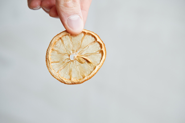 A dried orange slice with a stone held in a hand against a white background