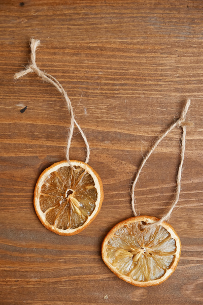 Two dried citrus slices with stones and with loops of twine are lying on a wooden table