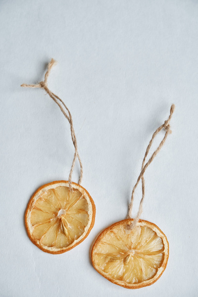 Dried edible citrus decorations for a Christmas tree on loops of twine on a white surface