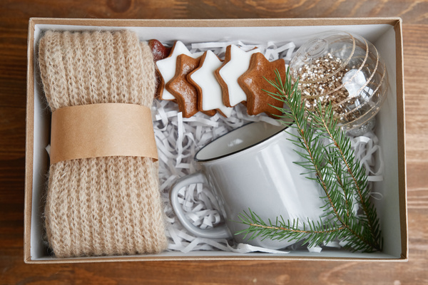A gift set consisting of a Christmas bauble a knitted item of clothing gingerbread and mugs decorated with a Christmas tree branch on the table