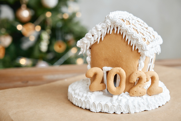 Gingerbread house decorated with cream and numbers symbolizing the coming year on a table with a Christmas tree on the background